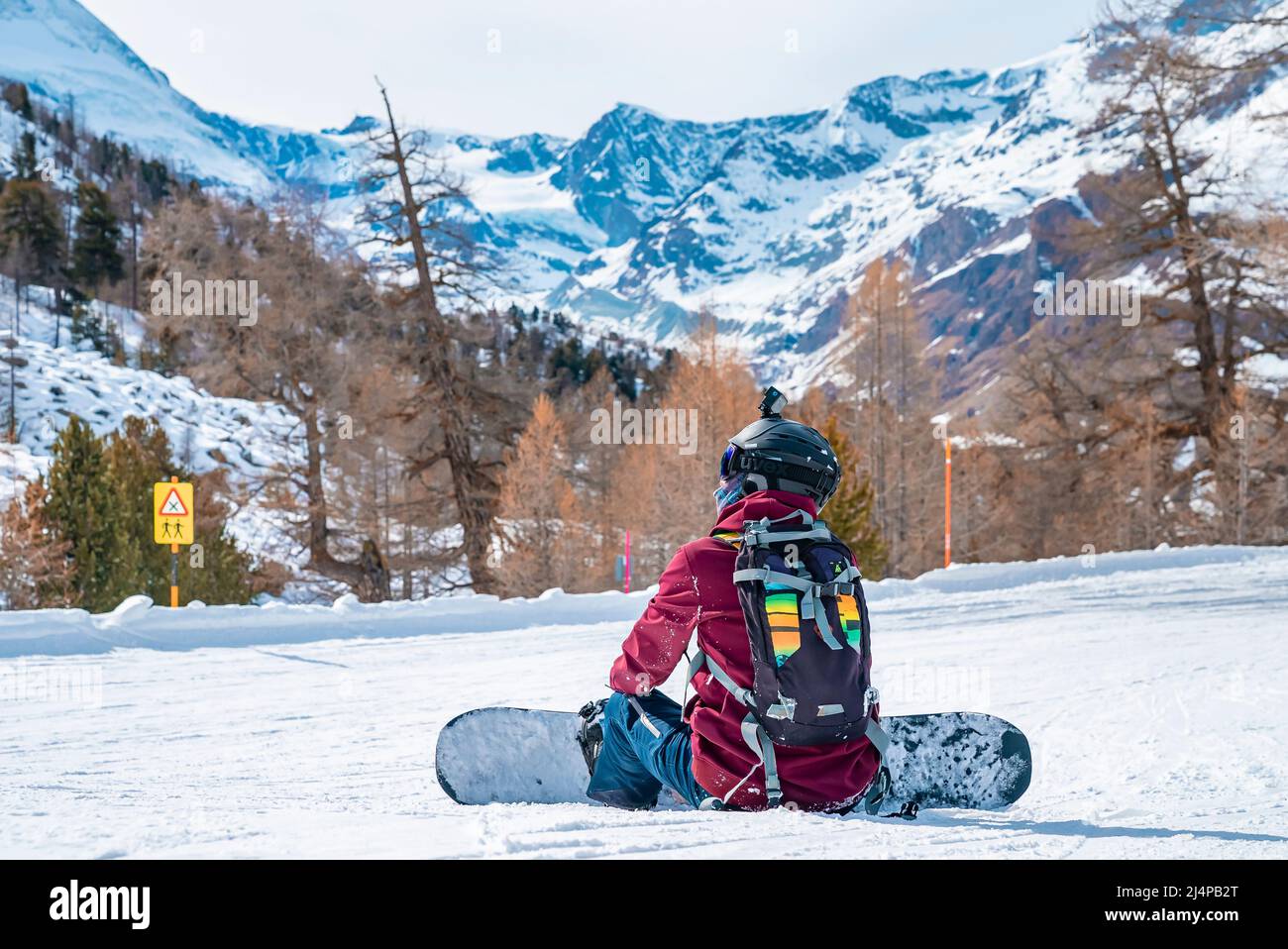 Tired snowboarder sitting on snow covered landscape while looking at mountains Stock Photo