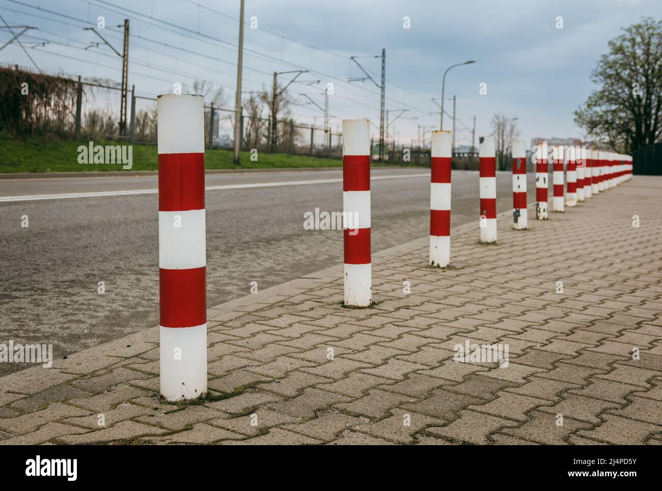Metal poles are located on the edge of the sidewalk. These are painted in red and white stripes. Stock Photo