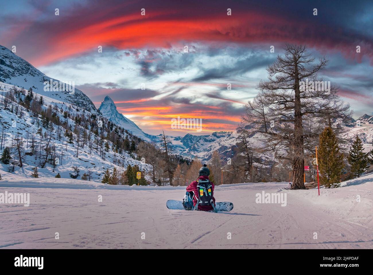Tired snowboarder sitting on snowy landscape looking at Matterhorn during sunset Stock Photo
