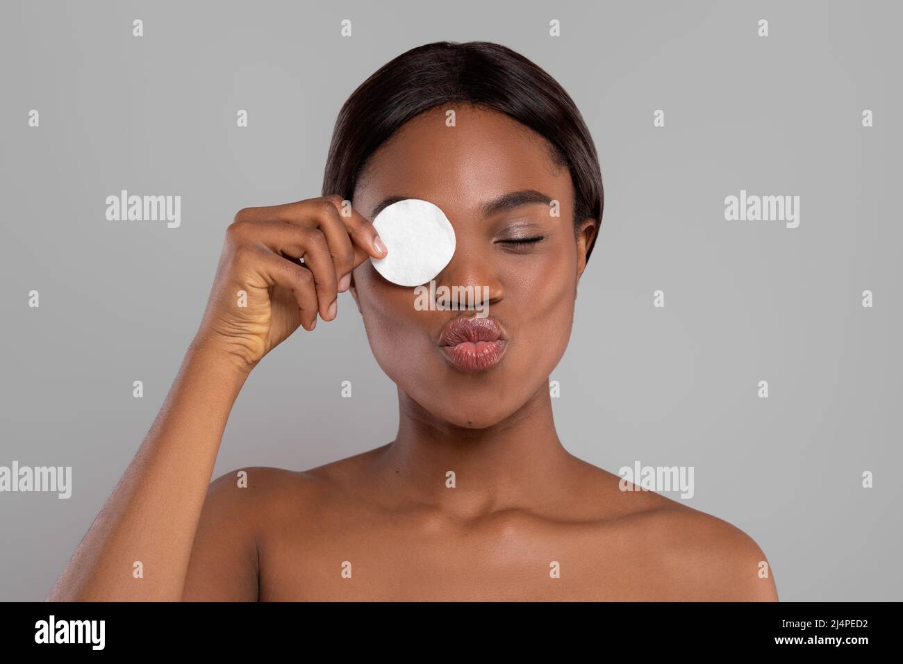 Glad black female with perfect skin doing air kiss, remove makeup with cotton pad, isolated on gray background Stock Photo