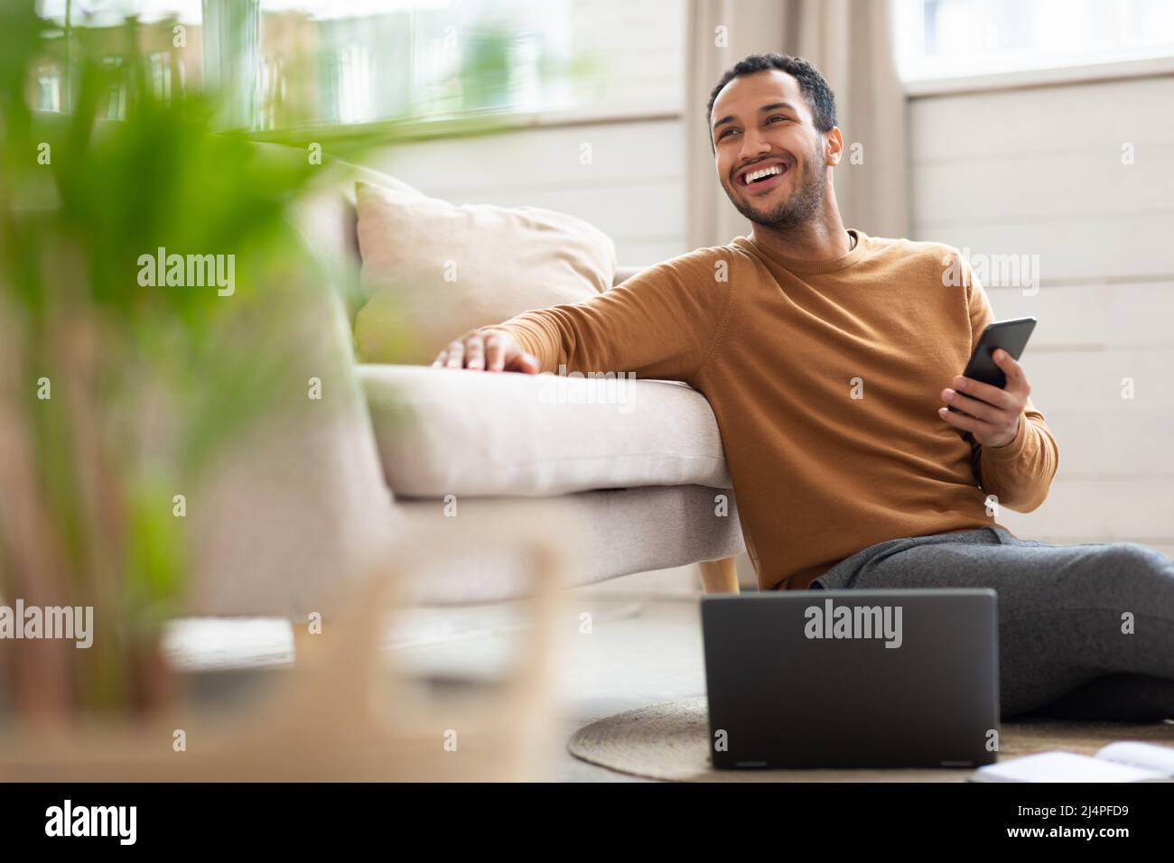 Young Arab man holding phone using pc at home Stock Photo