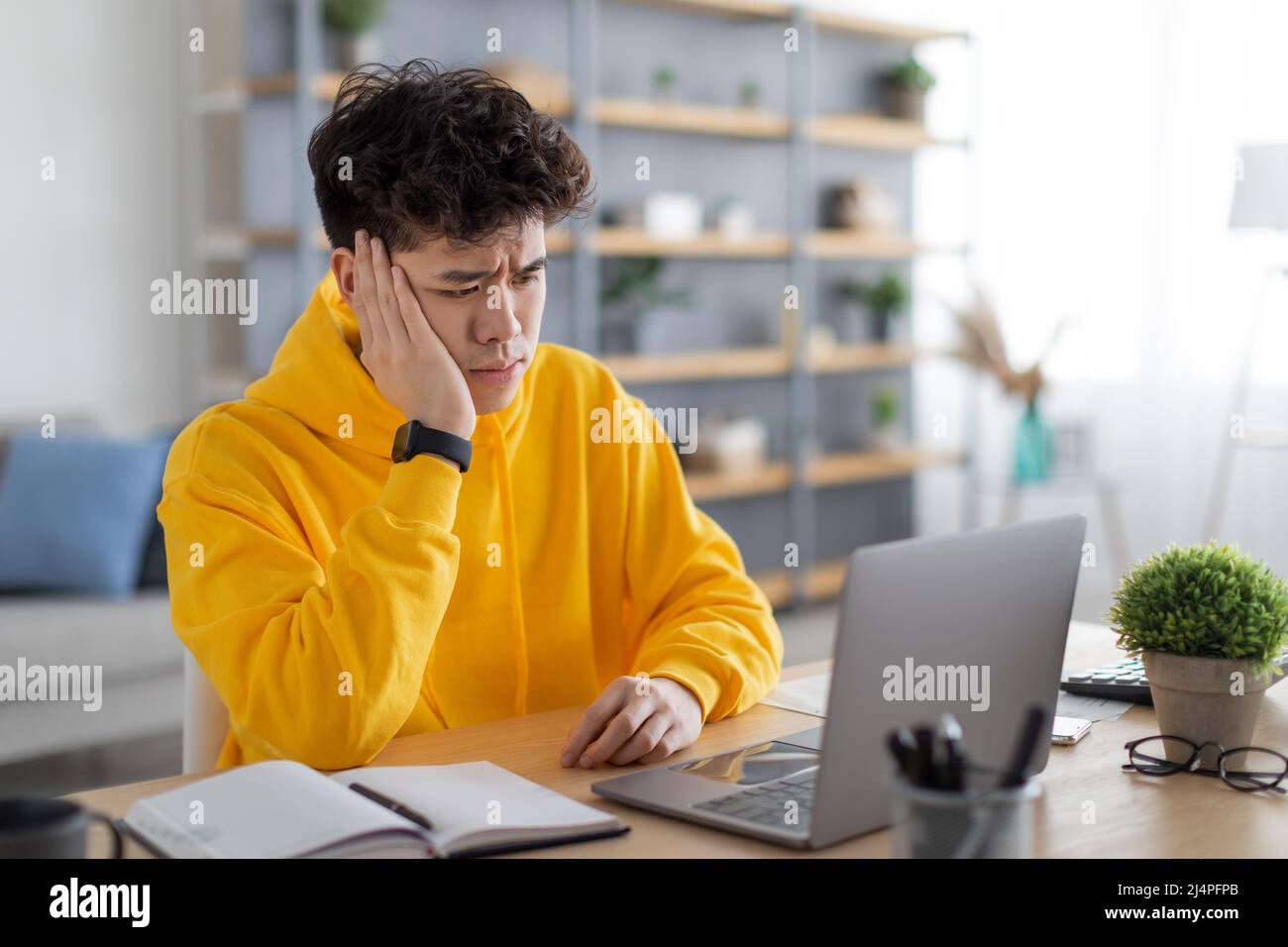 Bored Asian male student sitting at desk with pc Stock Photo