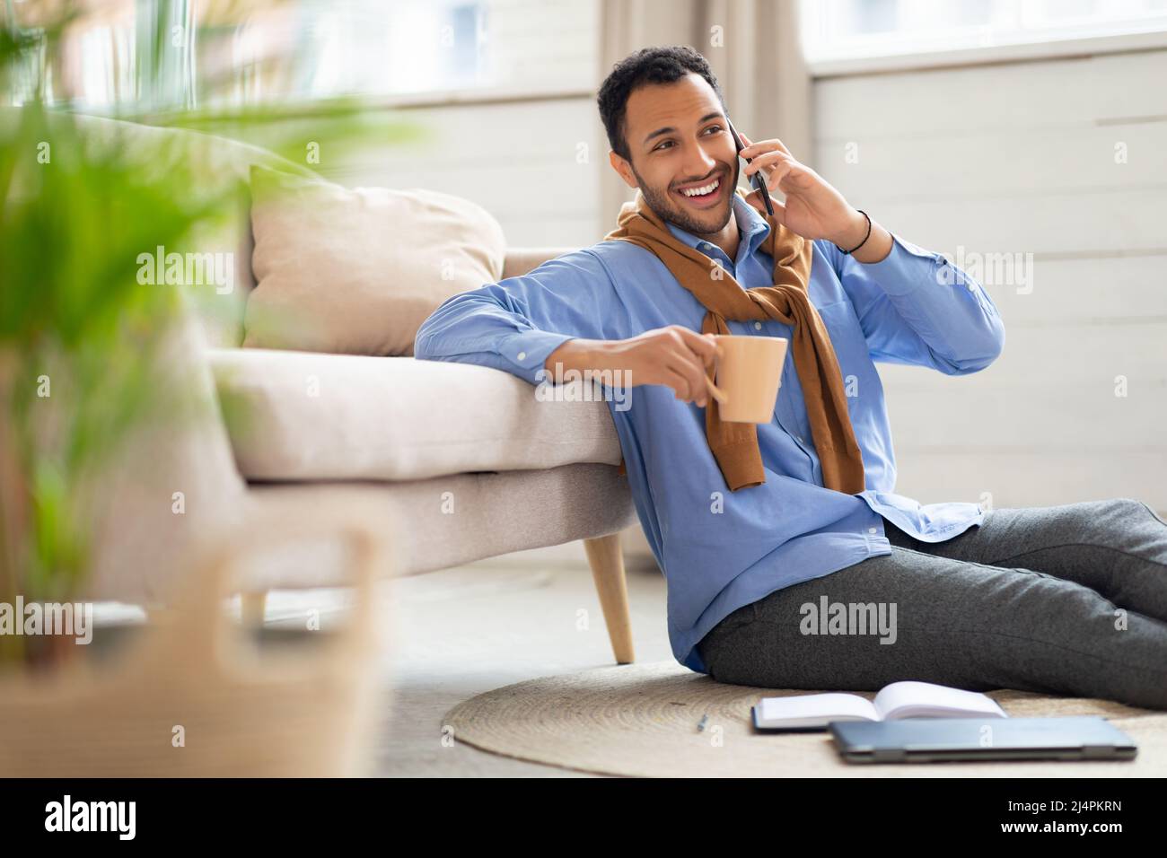 Smiling man talking on phone at home, drinking coffee Stock Photo