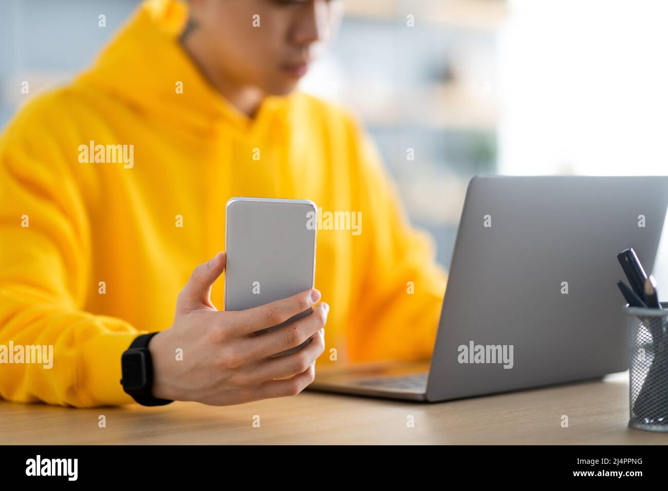 Asian man sitting at desk using cell phone, closeup Stock Photo