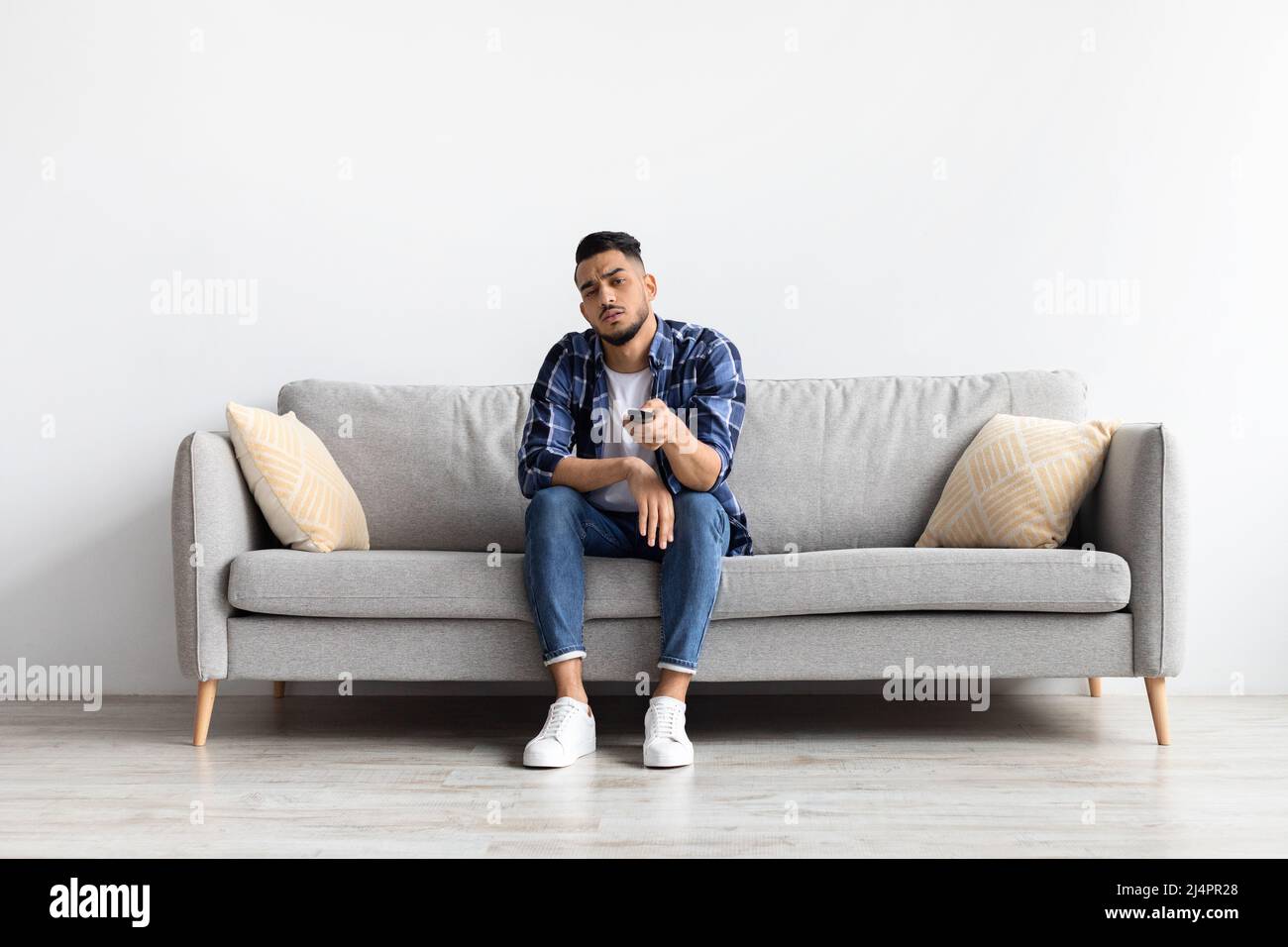 Bored young man watching television sitting on couch Stock Photo