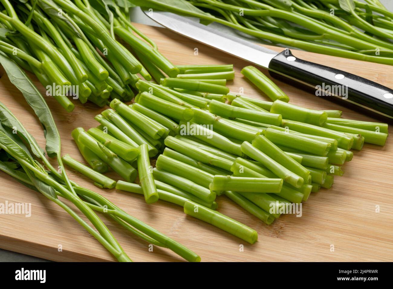 Fresh raw green pieces hollow water spinach,  kangkong, on a wooden cutting board close up Stock Photo