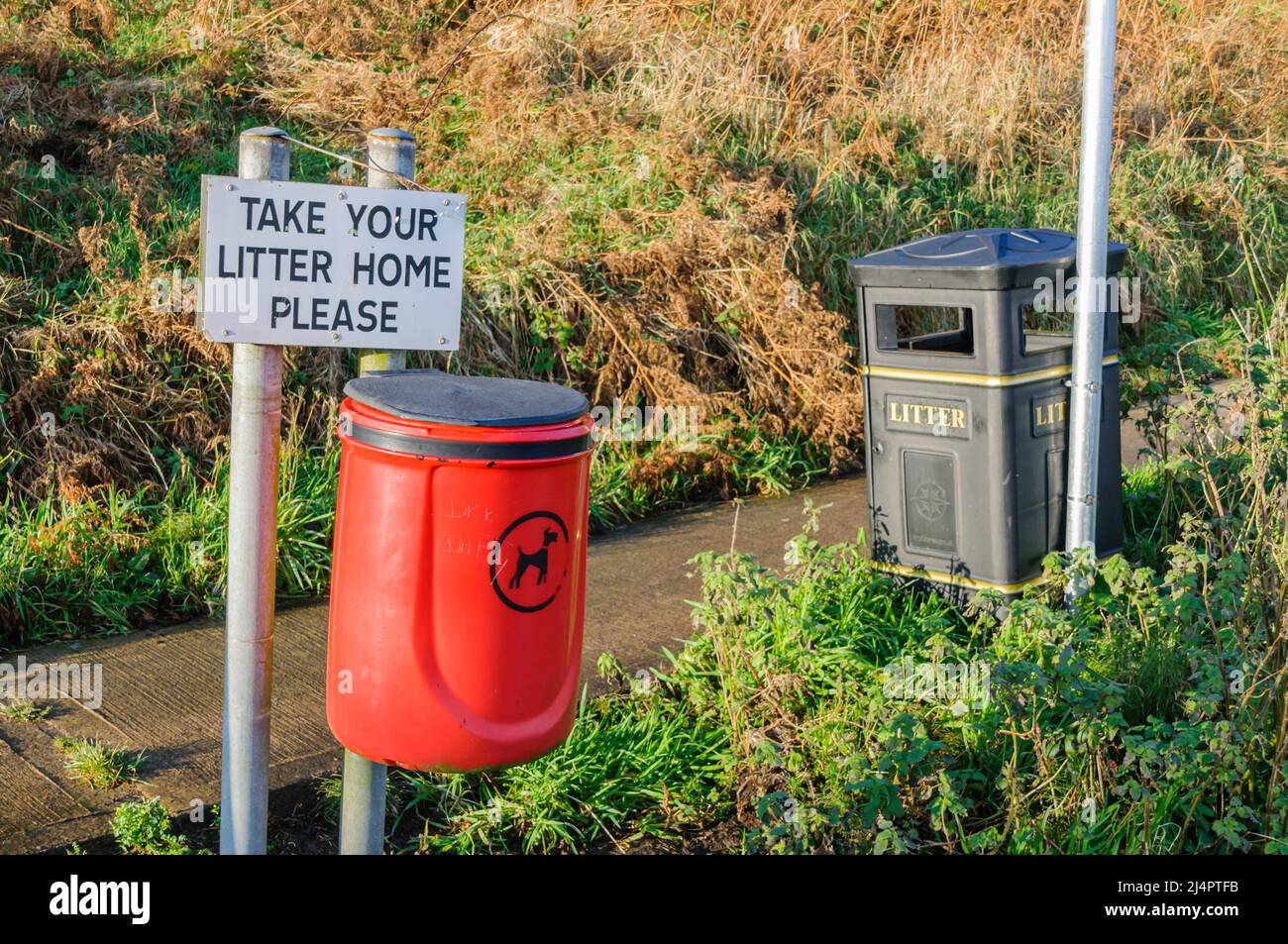 Sign asking park visitors to take their litter home, with a dog waste bin, and a litter bin. Stock Photo