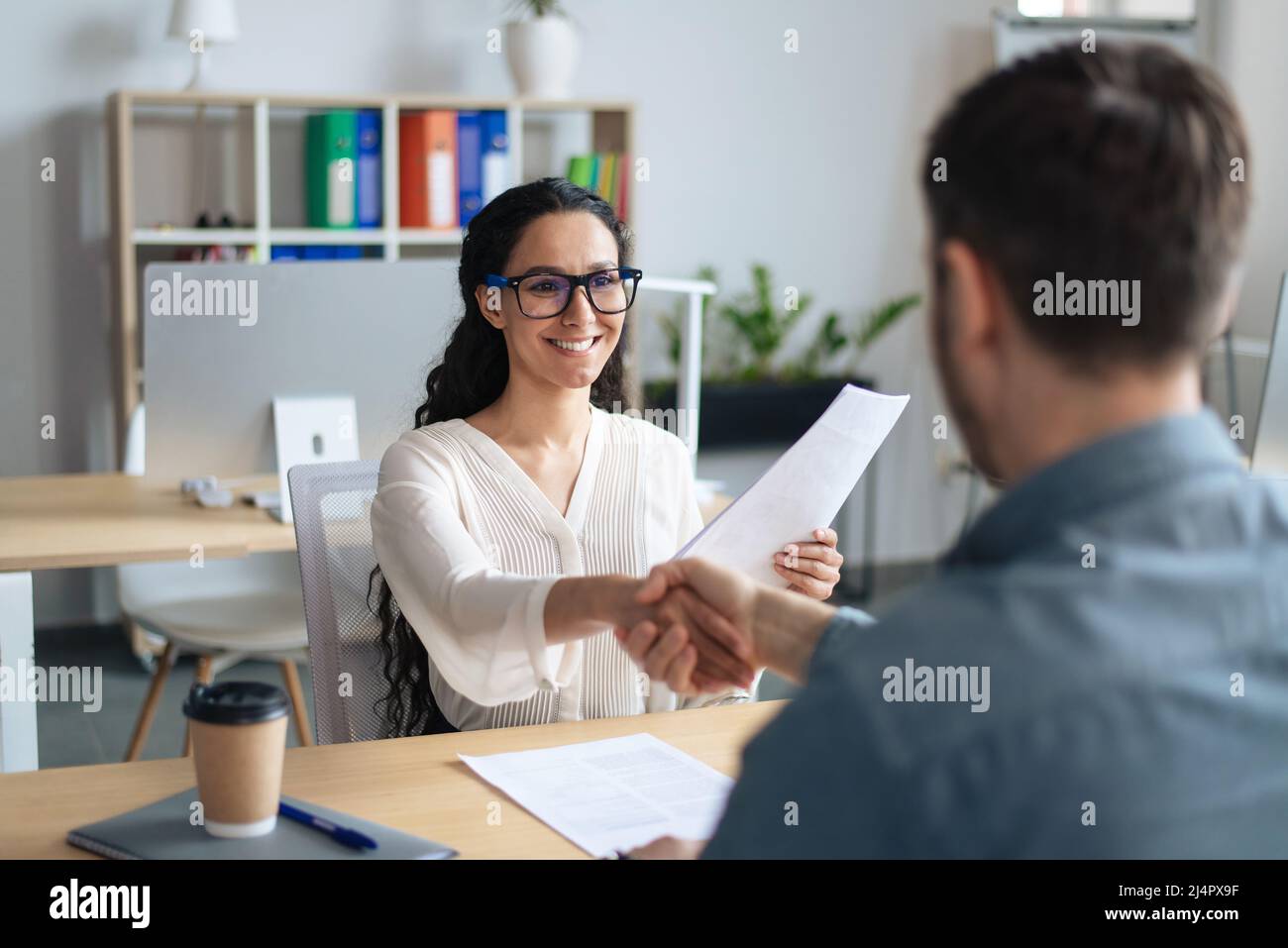 Smiling female personnel manager and job applicant shaking hands after successful employment interview at office Stock Photo