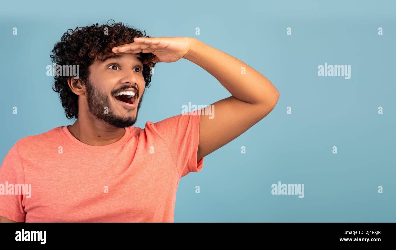 Excited hindu guy looking at copy space on blue Stock Photo