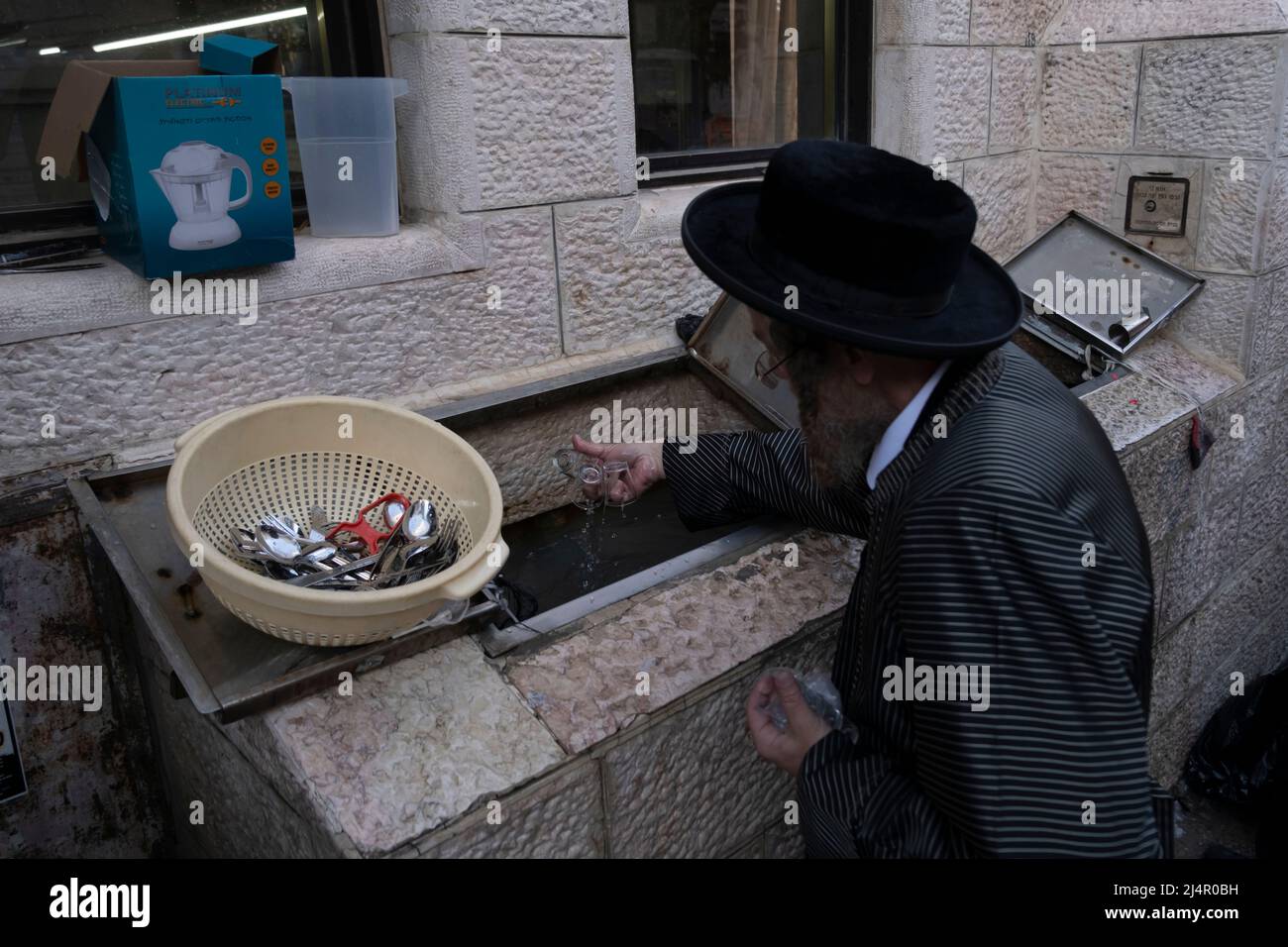 Ultra-Orthodox Jews immerse new purchased cooking utensils, prior to their first use, in a container with mikveh or well water in a process called Tevilat Keilim (Immersing Utensils) as they prepare for Pesach (Passover) in the religious neighborhood of Mea Shearim in Jerusalem, Israel. A central law of Passover observance is to remove all traces of hametz, meaning 'leaven' in Hebrew, which is forbidden on the Jewish holiday of Passover. Stock Photo