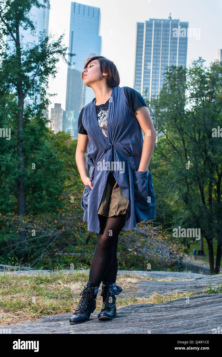 https://c8.alamy.com/comp/2J4R1CE/dressing-in-a-blue-sleeveless-long-blouse-black-leggings-and-boots-two-hands-putting-in-pockets-a-young-chinese-girl-is-standing-in-a-small-words-2J4R1CE.jpg