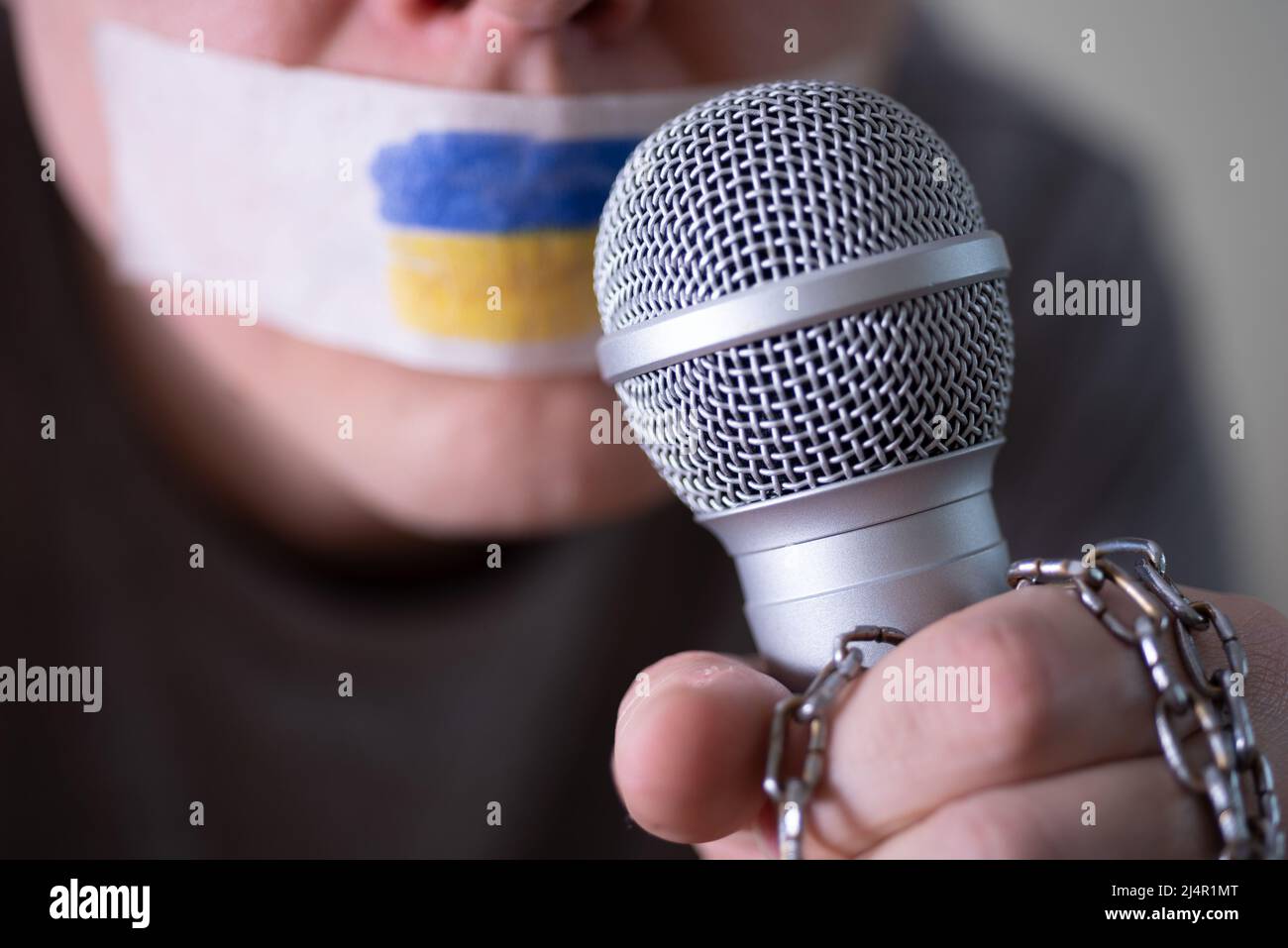 Tape over his mouth with the flag of Ukraine, trying to speak into a microphone. The concept of freedom of the press in Ukraine. Stock Photo