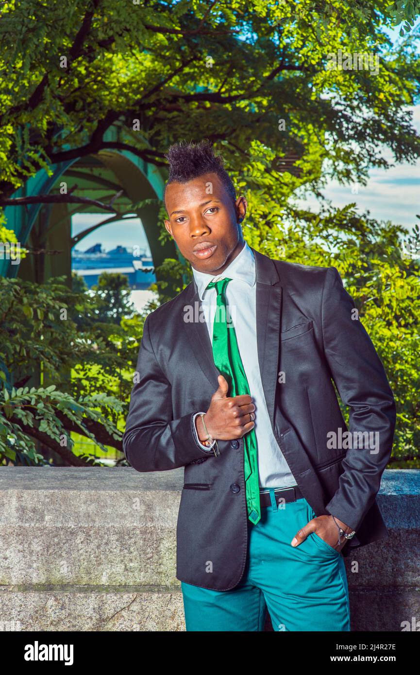 Urban Fashion. Dressing in a black blazer, green necktie, white undershirt, green  pants, a young black guy with mohawk hair is standing by a rocky fe Stock  Photo - Alamy