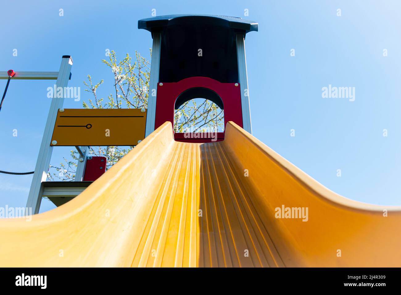 Brightly colored yellow playset with a slide and climbing frame in a playground for children who play Stock Photo