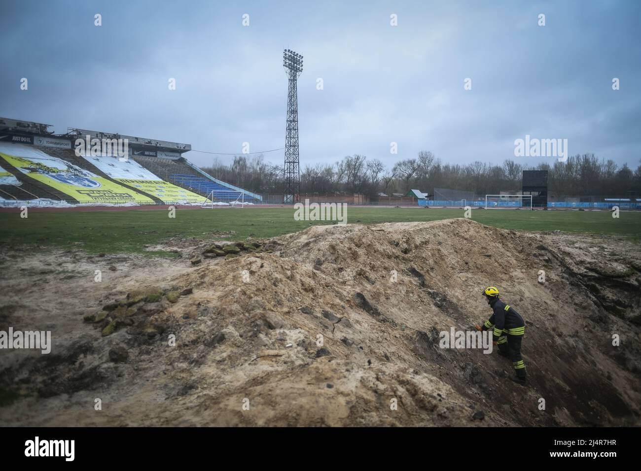 A fire fighter inspects a crater in a football pitch at the stadium a residential area of Chernihiv, Ukraine damaged by shelling during the Russian invasion on April 16, 2022. Russian military forces entered Ukraine territory on Feb. 24, 2022. (Photo by Piero Cruciatti/Sipa USA) Stock Photo