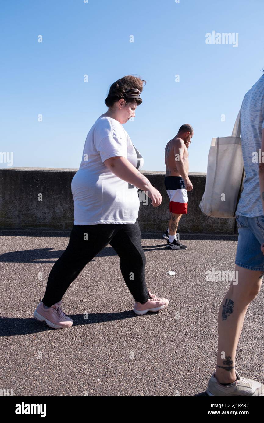 Two men and a woman busily walking by the seaside at Clacton on Sea, Essex. Stock Photo