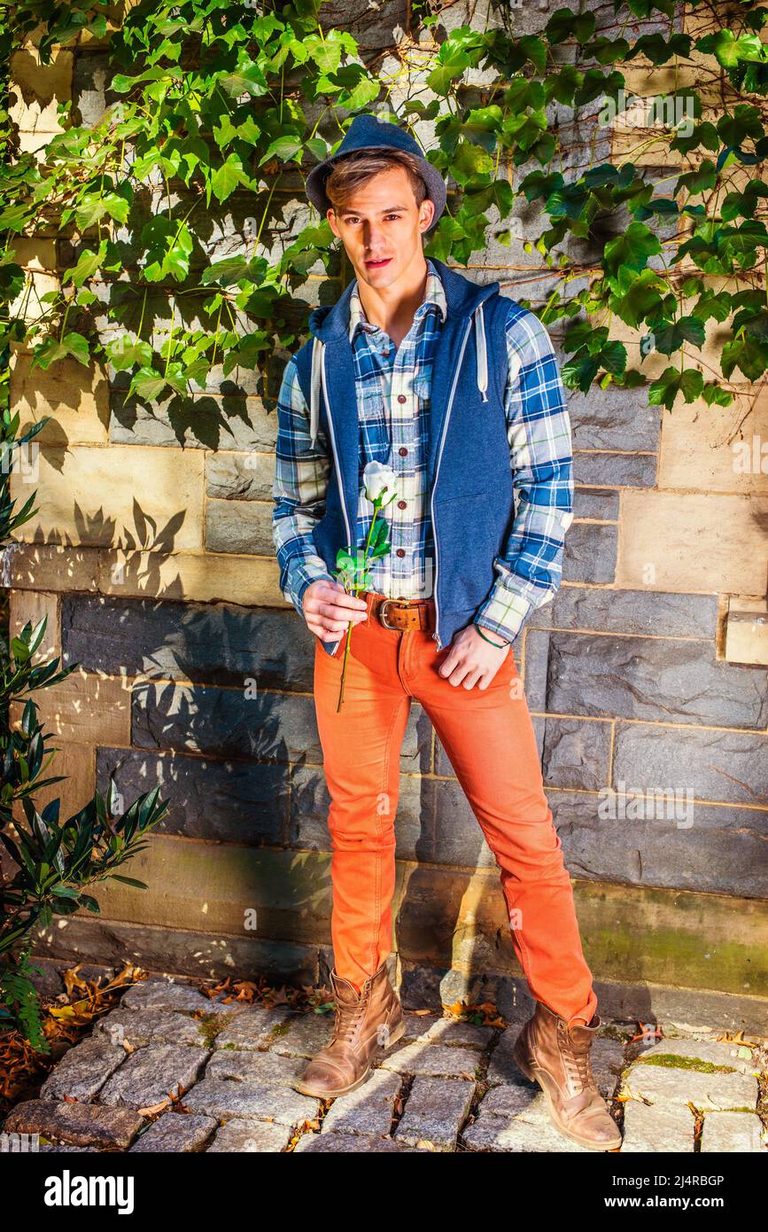 Man waiting for you. Dressing in blue, white pattern shirt, blue hoodie vest,  red jeans, brown leather boot shoes, wearing woolen Fedora hat, a young Stock Photo