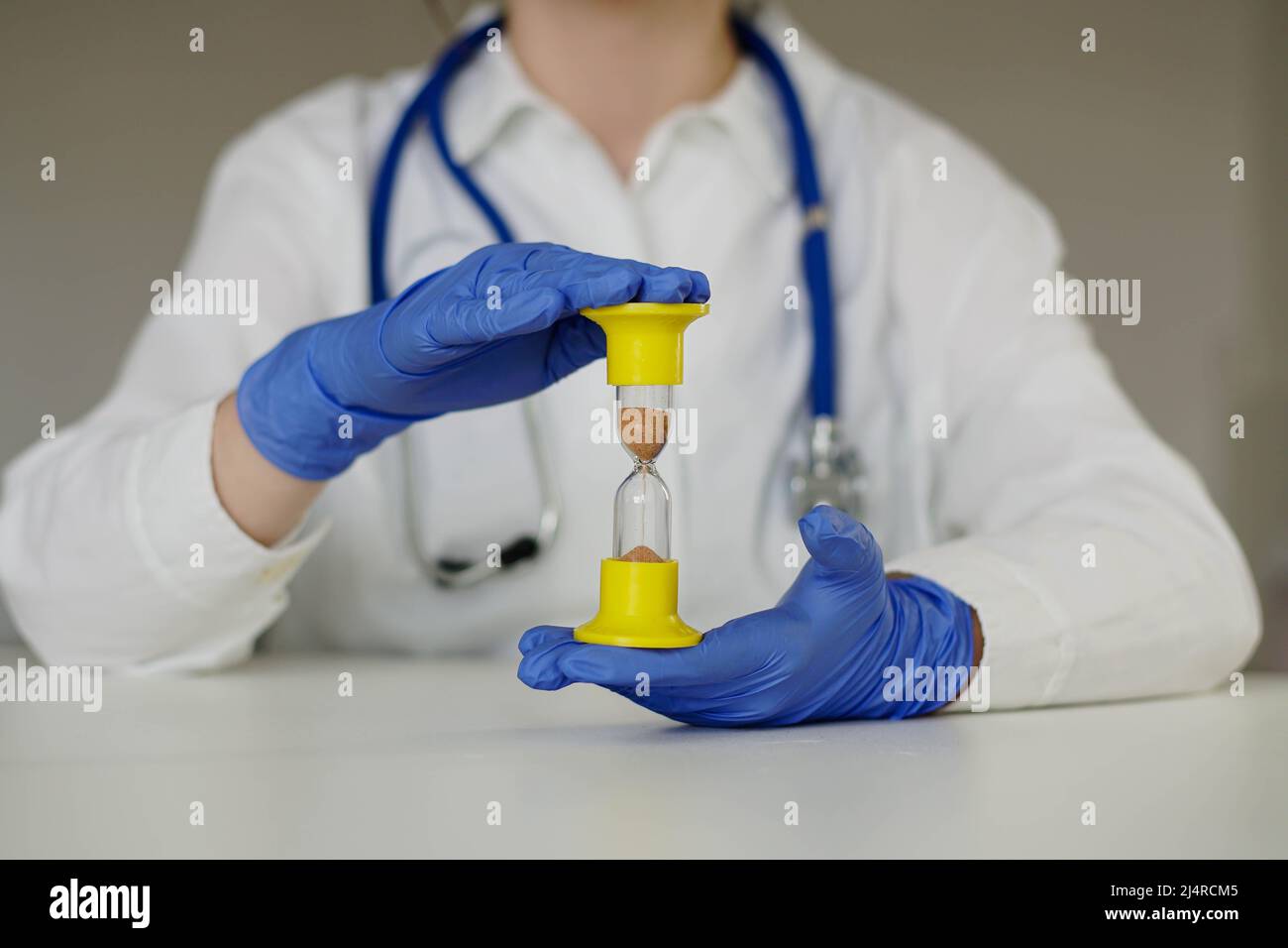 Overtime working hours of medical worker. Doctor in blue gloves holds an hourglass. Stock Photo