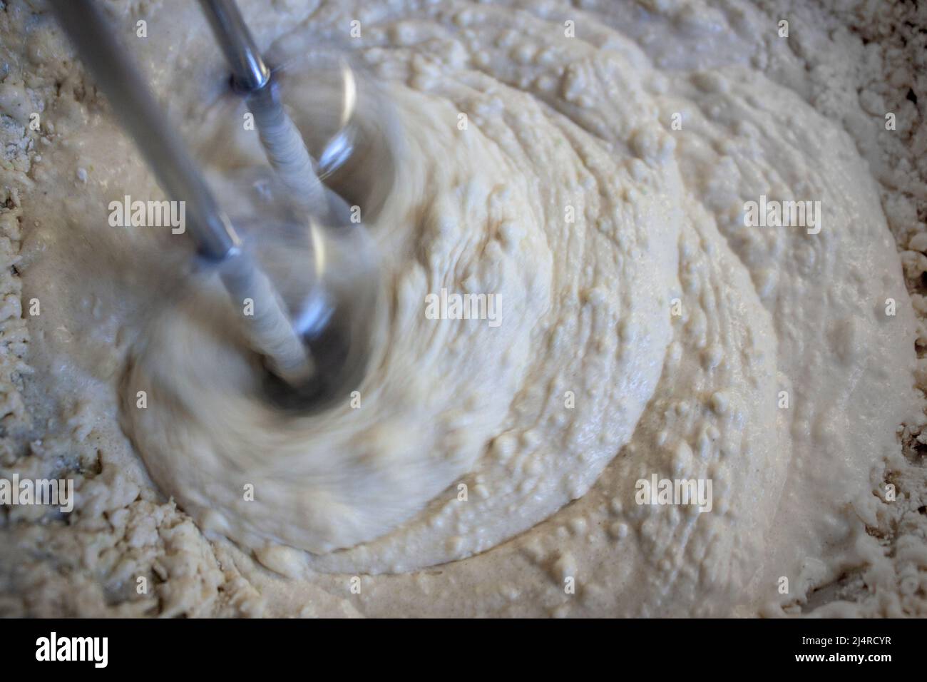 Beaters of electric mixer beating lumpy batter in a bowl Closeup and