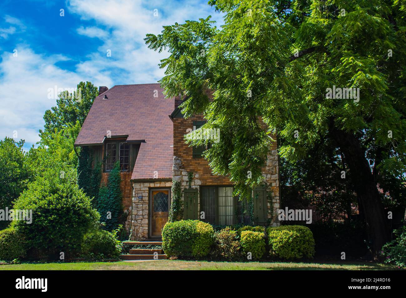 Beautiful stone two story cottage with green shutters and a steep roof