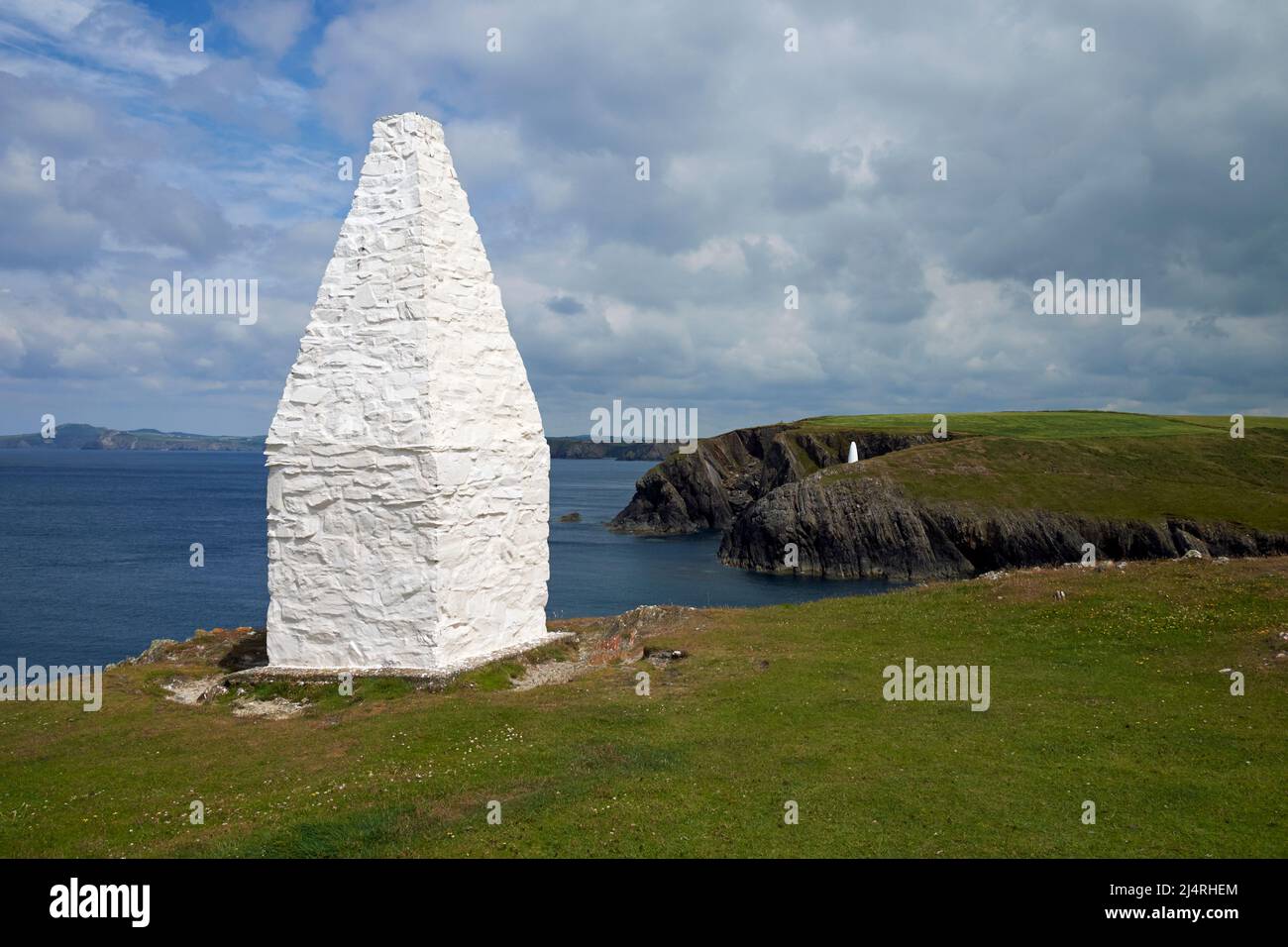 A whitewashed stone cairn marking the harbour at Porthgain, Pembrokeshire, Wales, UK. A second cairn can be seen on the opposite clifftop. Stock Photo