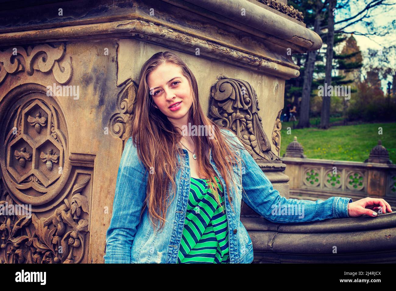 American teenage girl wearing patterned undershirt, Denim jacket, leaning against column of old