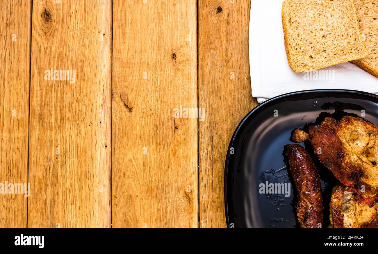 Pork chops with condiments and smoked sausage on a black plate, over