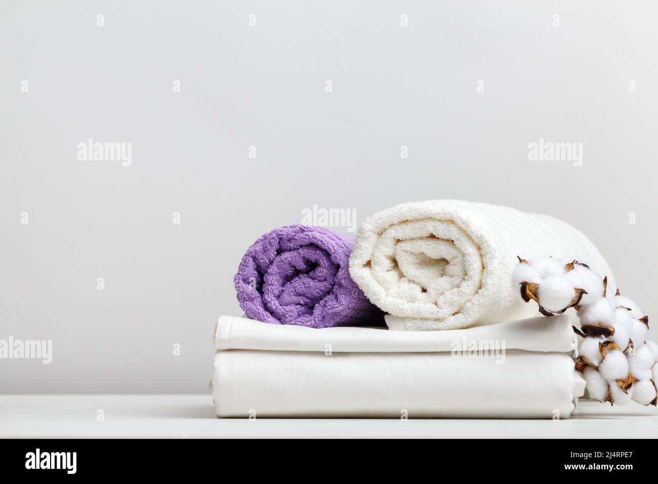 White bed linen, sheets and terry towels with a cotton branch on a light gray table Stock Photo