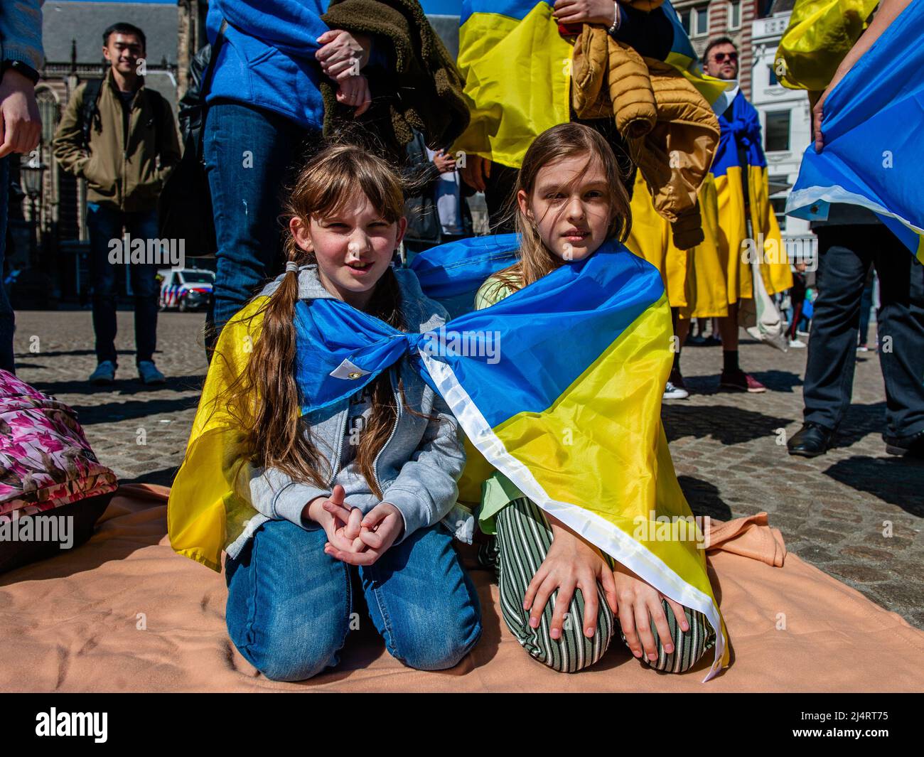 Amsterdam, Netherlands. 17th Apr, 2022. Two little Ukrainian girls wrapped  with a flag are seen kneeling on the ground during the demonstration. The  Ukrainian community in The Netherlands performed in the city