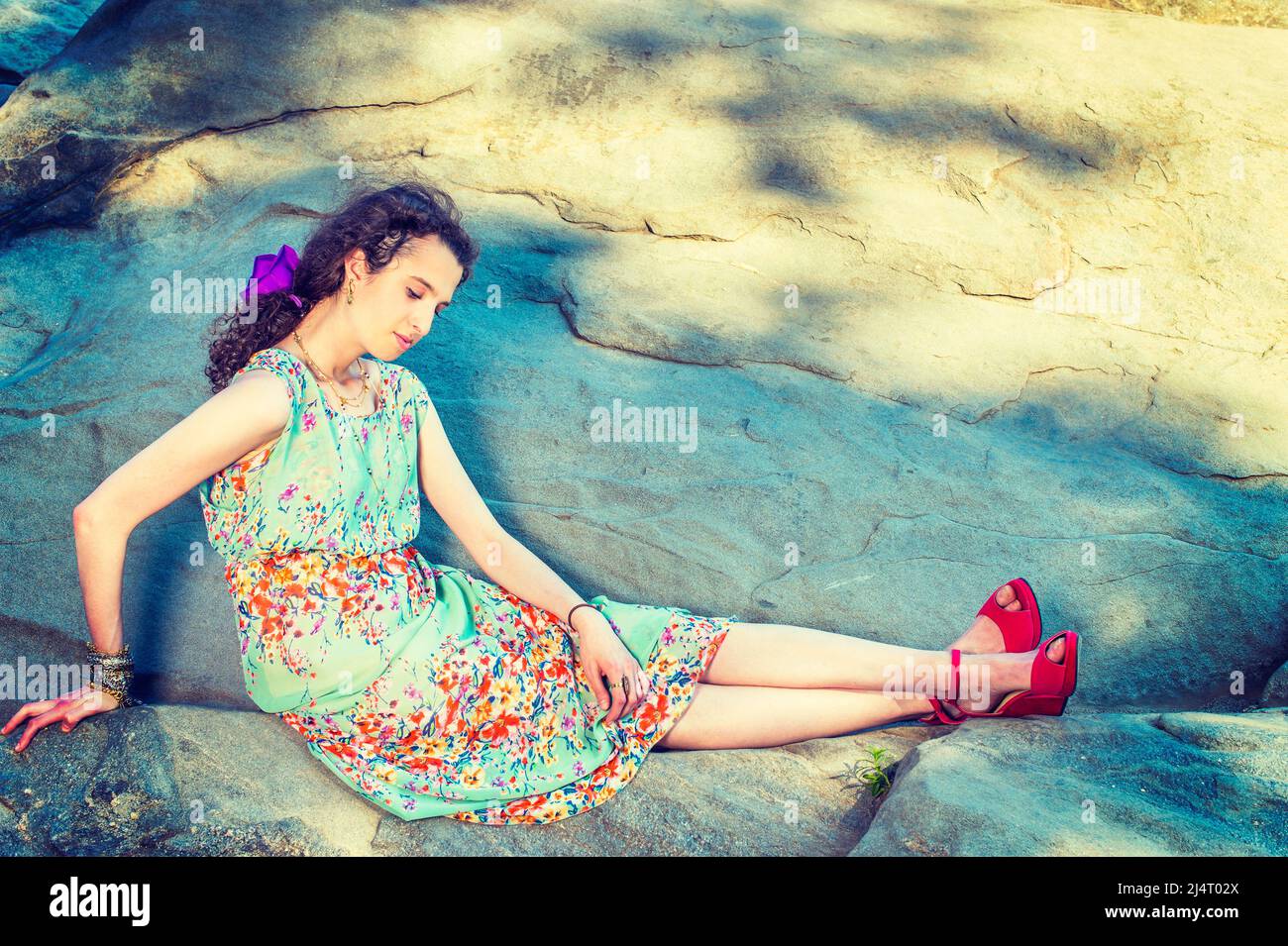 Summer Fashion. Dressing in sleeveless, long dress, red sandals shoes, purple flower hairpin,  chunky chain bracelet, a beautiful teenage girl is sitt Stock Photo