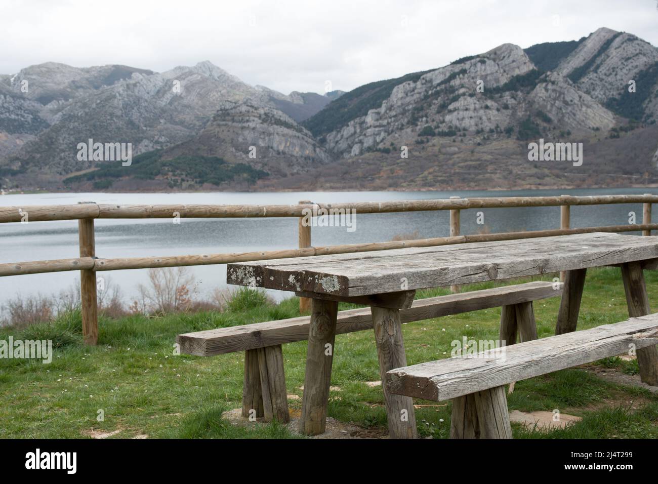 Picnic area with wooden table and bench. Magnificent view of the water reservoir at Caldas de Luna and the mountains around. Natural park of Babia and Stock Photo