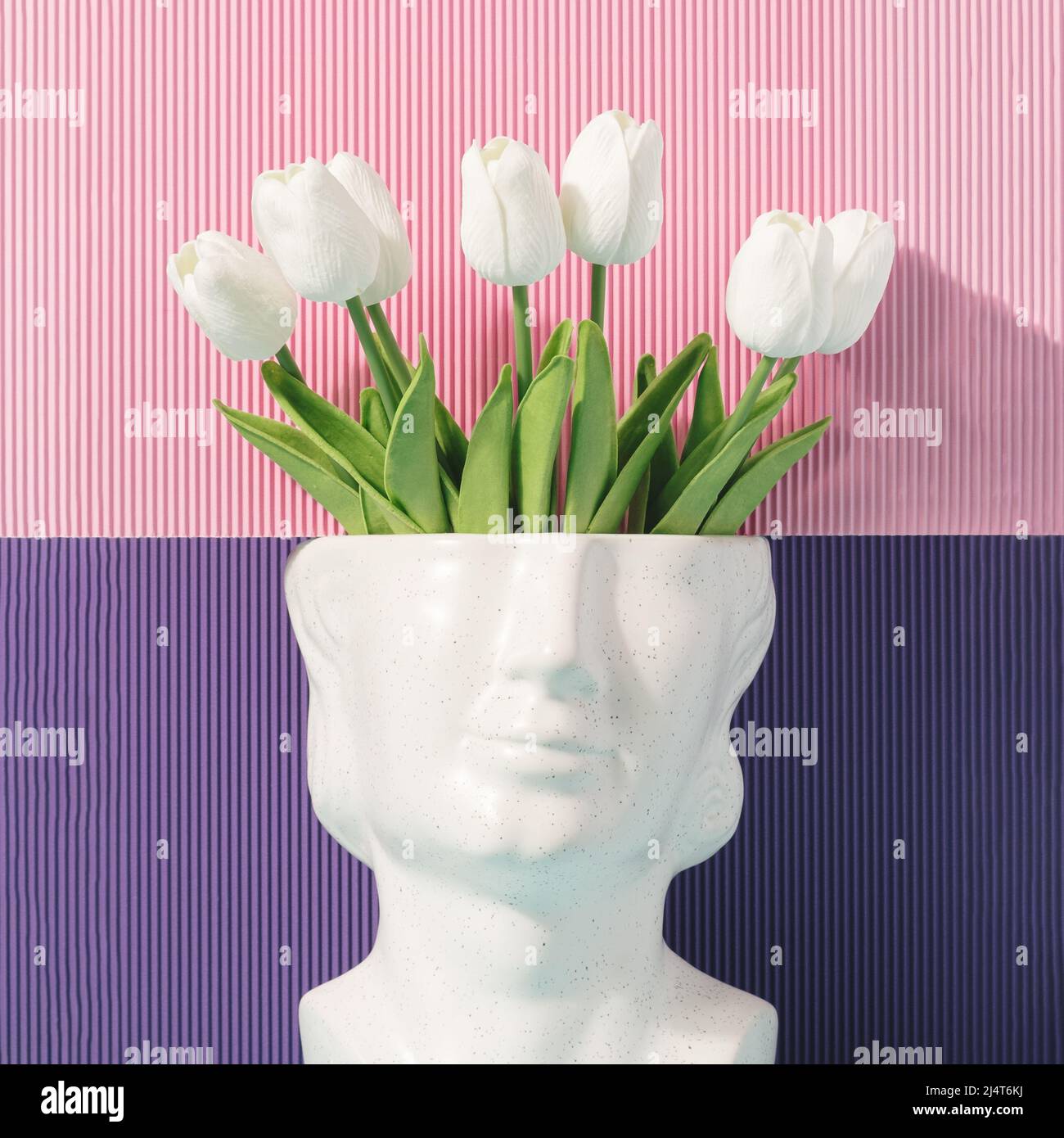Stone head sculpture with tulip flowers on a pink and purple background. Optimistic thoughts artistic concept. Stock Photo