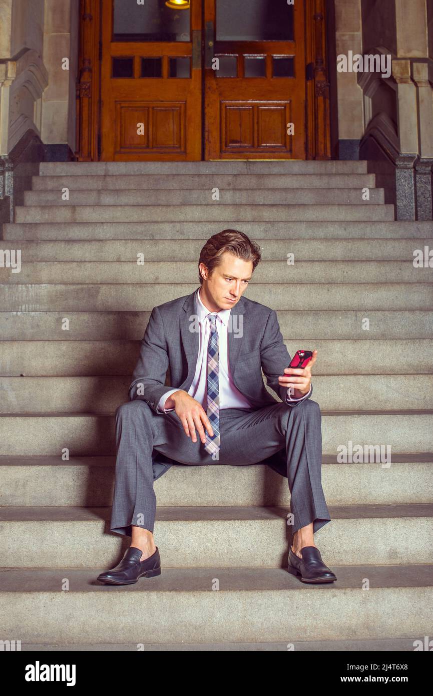 Businessman Waiting for You. Dressing formally in gray suit, white under shirt, patterned neck tie, a young businessman is casually sitting on steps o Stock Photo