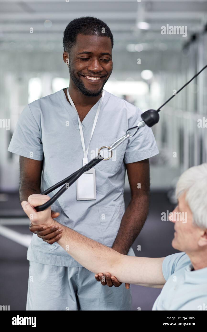 Vertical portrait of smiling rehabilitation therapist assisting senior man at gym in clinic Stock Photo