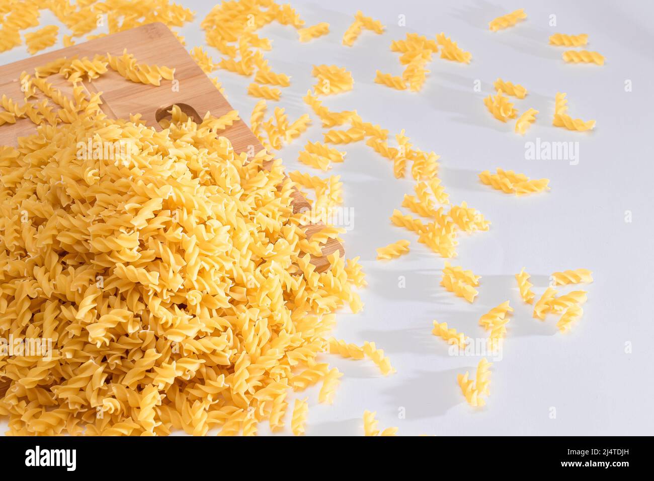 Uncooked Fusilli Pasta Scattered on Wooden Board and White Table. Raw