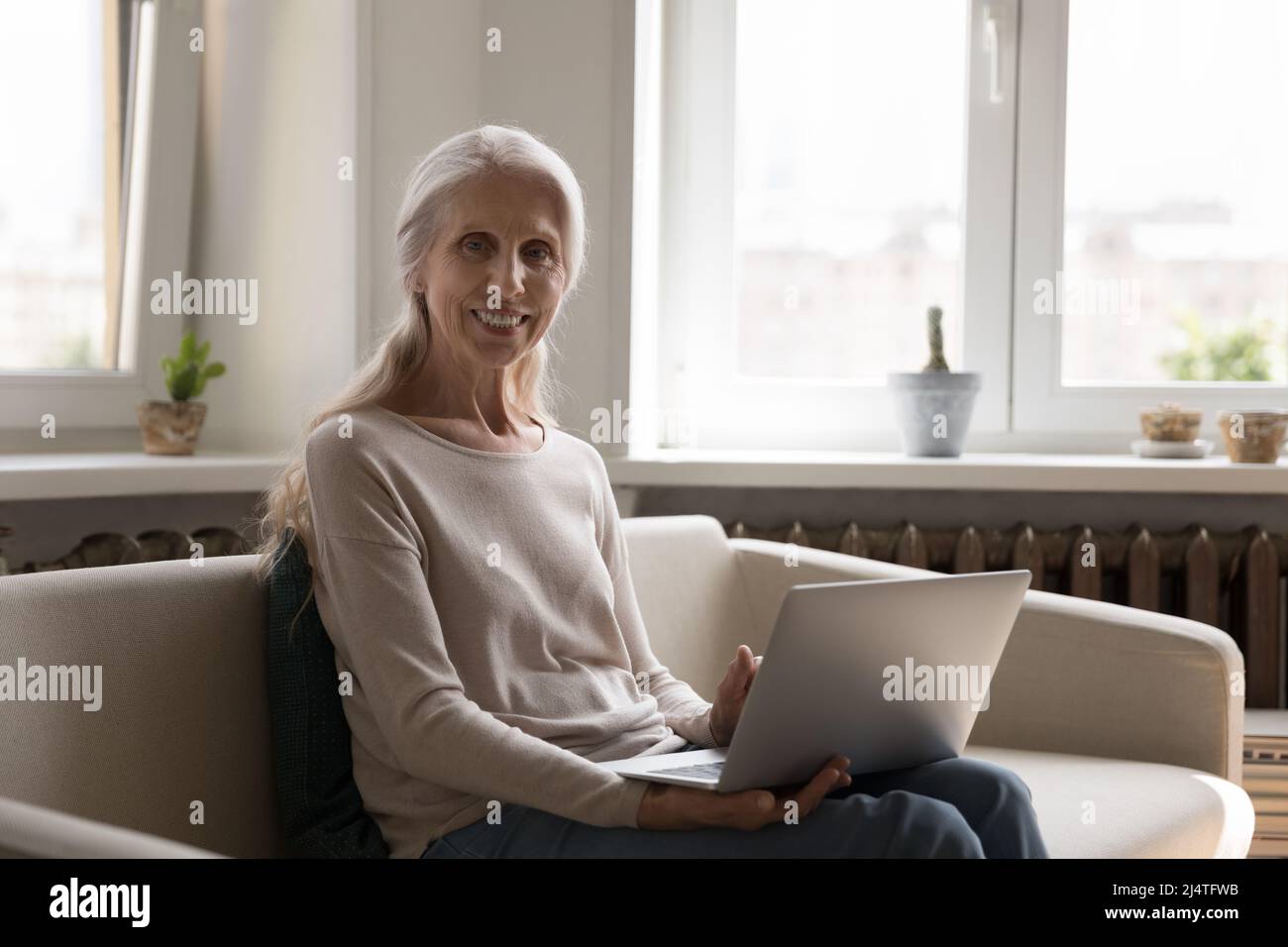 Mature woman sit on sofa with laptop looks at camera Stock Photo - Alamy