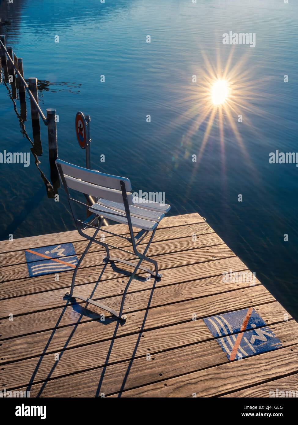 An empty chair on a wooden pier by Zug Lake, which reflects the sunstar Stock Photo