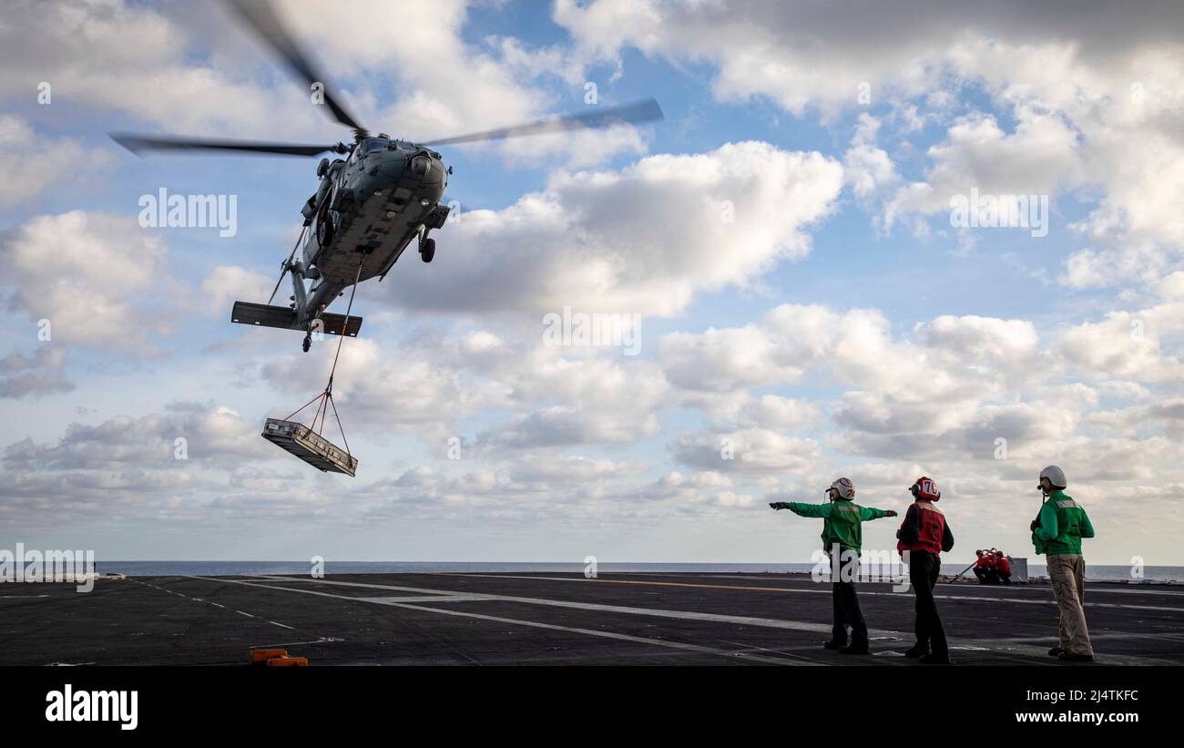 220416-N-SY758-1029 ATLANTIC OCEAN (April 16, 2022) An MH-60S Sea Hawk helicopter, attached to Helicopter Sea Combat Squadron (HSC) 7, deposits ammunition onto the flight deck of the aircraft carrier USS George H.W. Bush (CVN 77) during an ammunition onload with the dry cargo ship USNS William Mclean (T-AKE 12), April 16, 2022. George H.W. Bush provides the national command authority flexible, tailorable war fighting capability through the carrier strike group that maintains maritime stability and security in order to ensure access, deter aggression and defend U.S., allied and partner interest Stock Photo