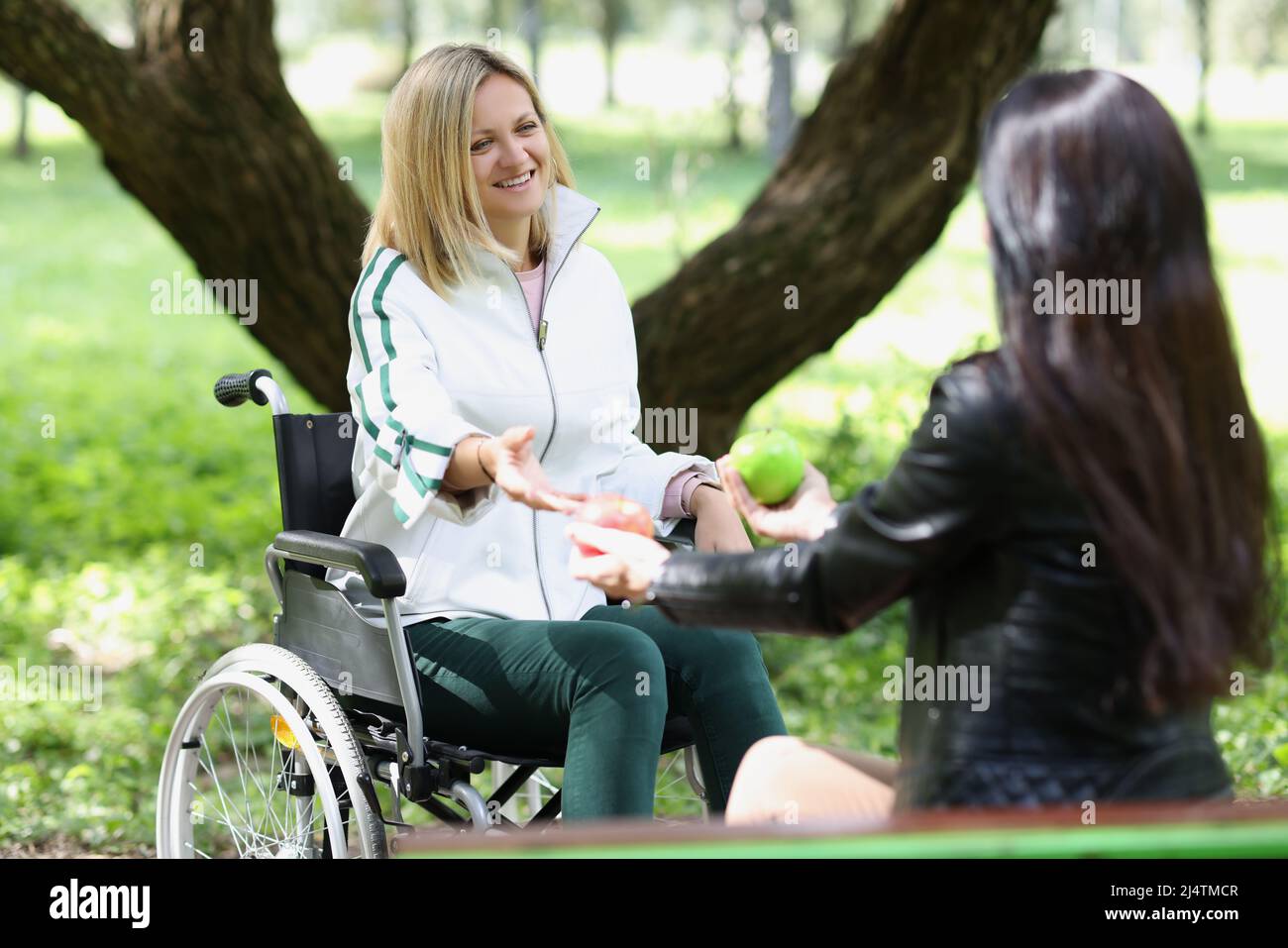 Woman communicates with friend in wheelchair in park Stock Photo - Alamy