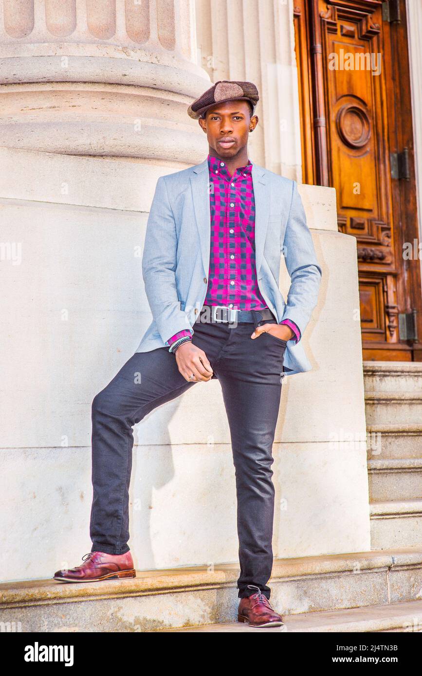Man Urban Fashion. Wearing fashionable Apple Newsboy cap, dressing in light gray blazer, patterned pink, black under shirt, black pants, brown leather Stock Photo