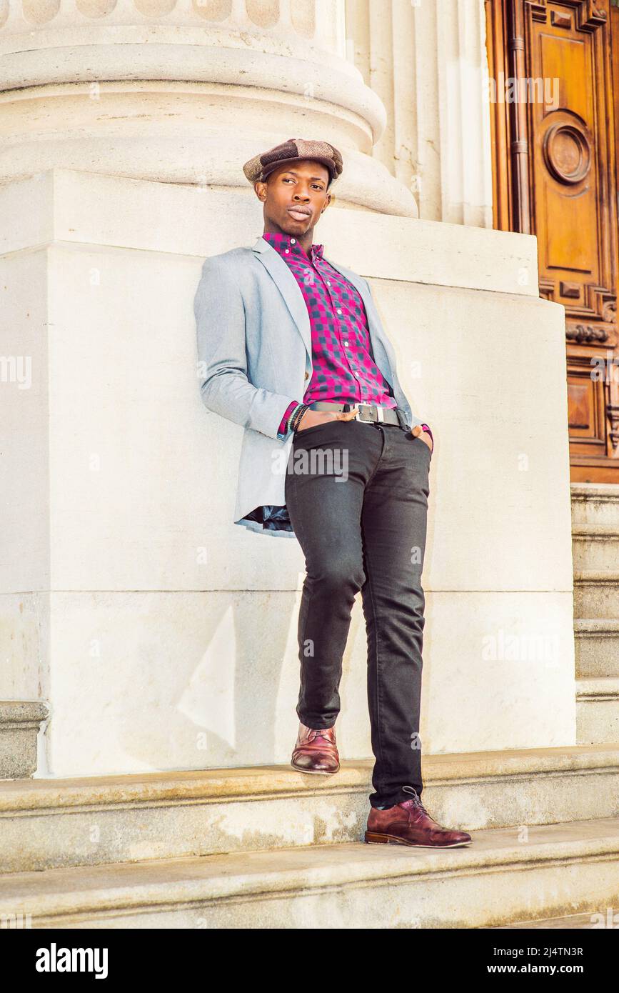 Man Urban Fashion. Wearing a  Newsboy cap, dressing in light gray blazer, patterned pink, black under shirt, black pants, brown leather shoes, a young Stock Photo