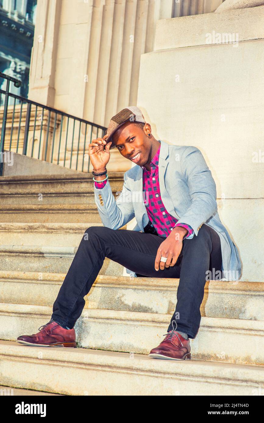 Man Urban Fashion. Wearing a Newsboy cap, dressing in light gray blazer, patterned pink, black under shirt, black pants, brown leather shoes, a young Stock Photo