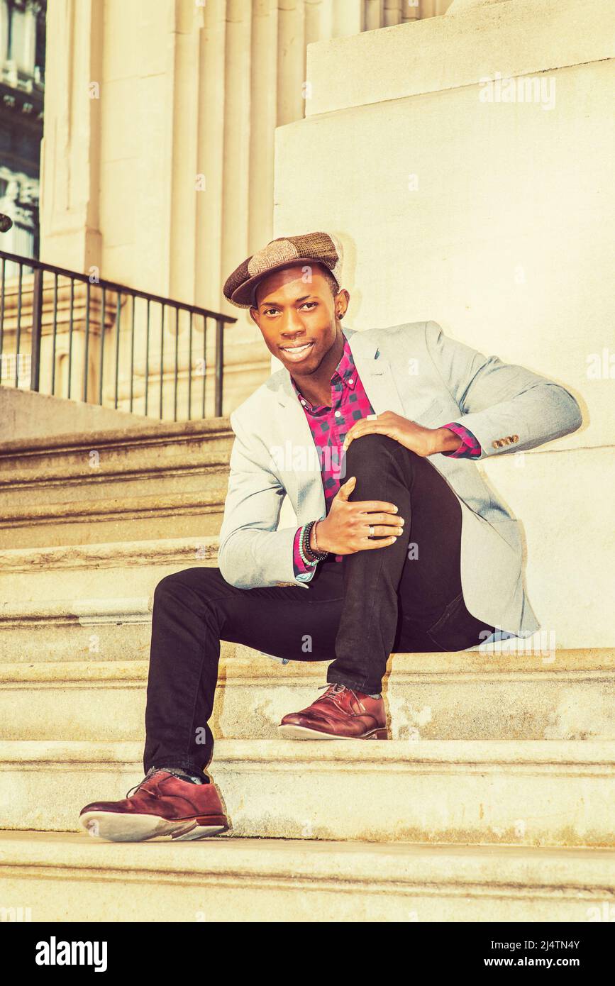 Man Urban Fashion. Wearing a Newsboy cap, dressing in light gray blazer, patterned pink, black under shirt, black pants, brown leather shoes, a young Stock Photo