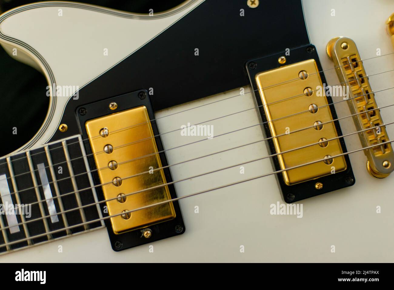Gibson guitar in white, black and gold with close-up of strings and pickups. Stock Photo