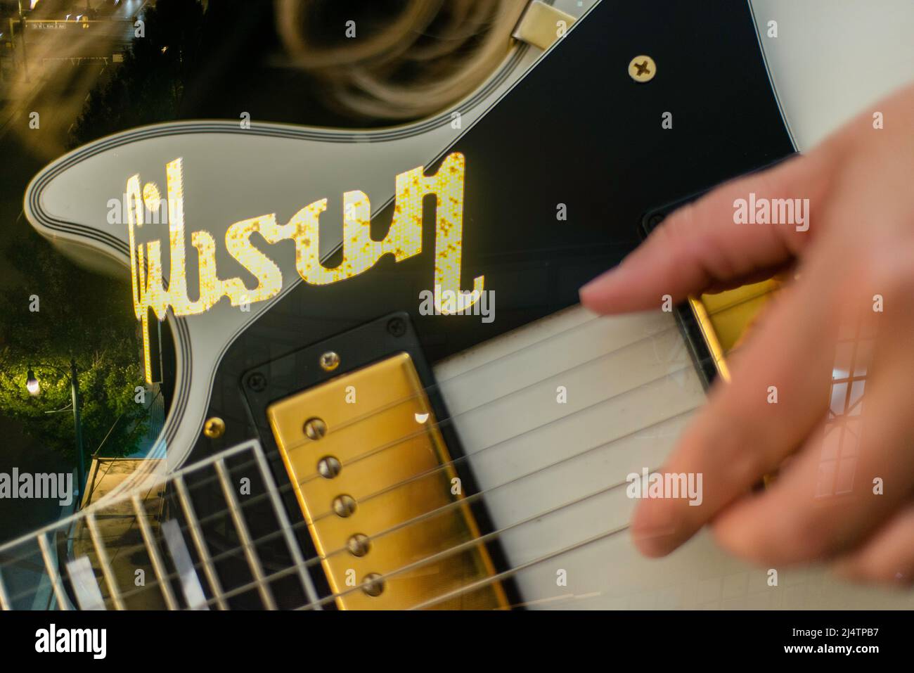 Blonde singer songwriter woman playing a white Gibson guitar with multi-exposure with lights from the Gibson guitar factory. Stock Photo