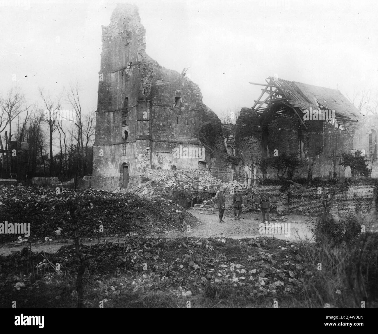 Ruined church and graveyard, during World War I. Three soldiers are visible at the foot of the photograph, although they are dwarfed by the size of the now destroyed church. The crosses in the yard at the side of the church are, poignantly, still standing. Stock Photo