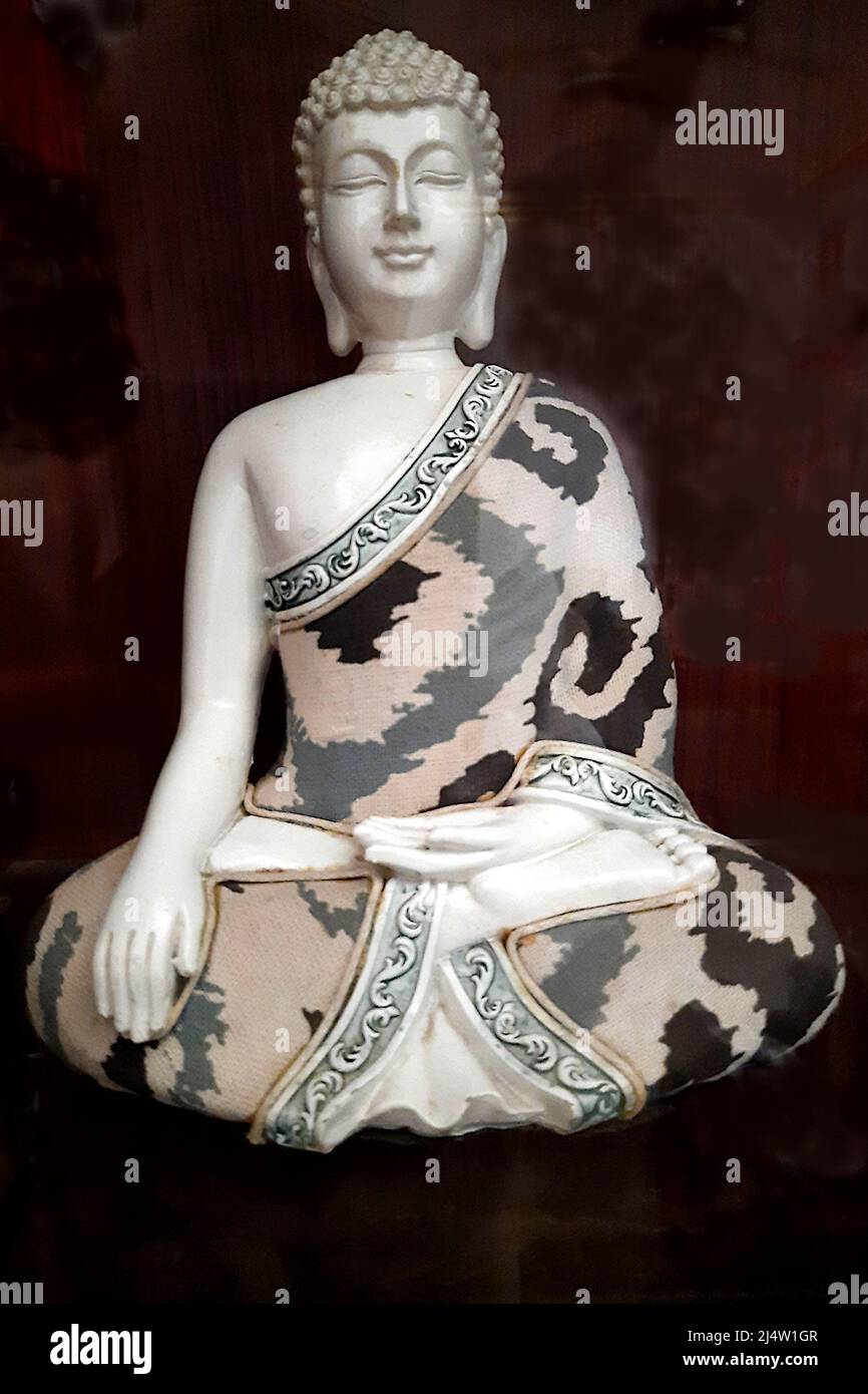 View of sculpture of Buddha in serene sitting pose wearing printed drapery against dark background Stock Photo