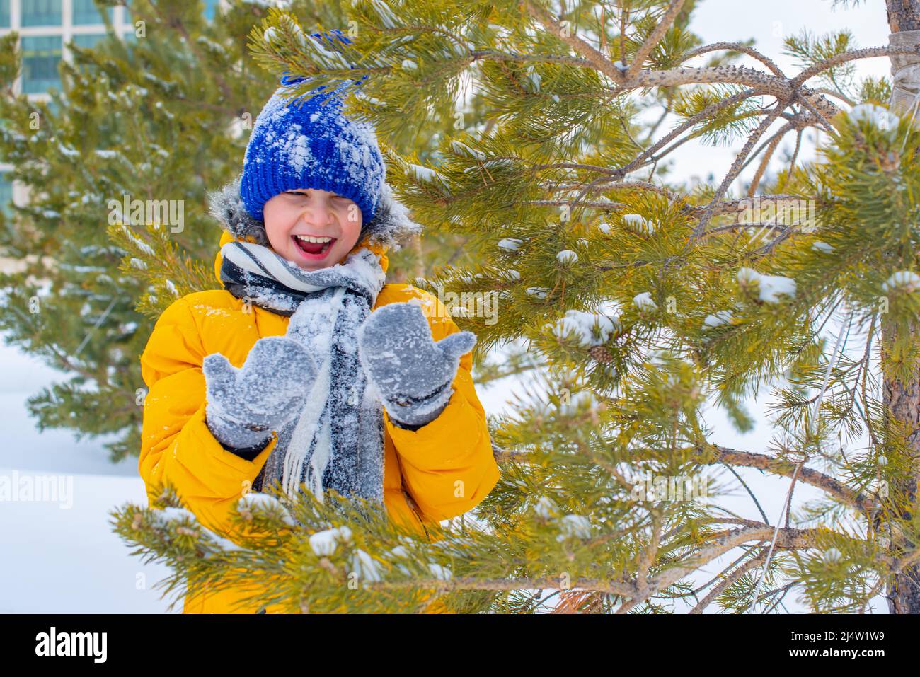 in a blue hat and a yellow jacket a cheerful boy in the snow Stock Photo
