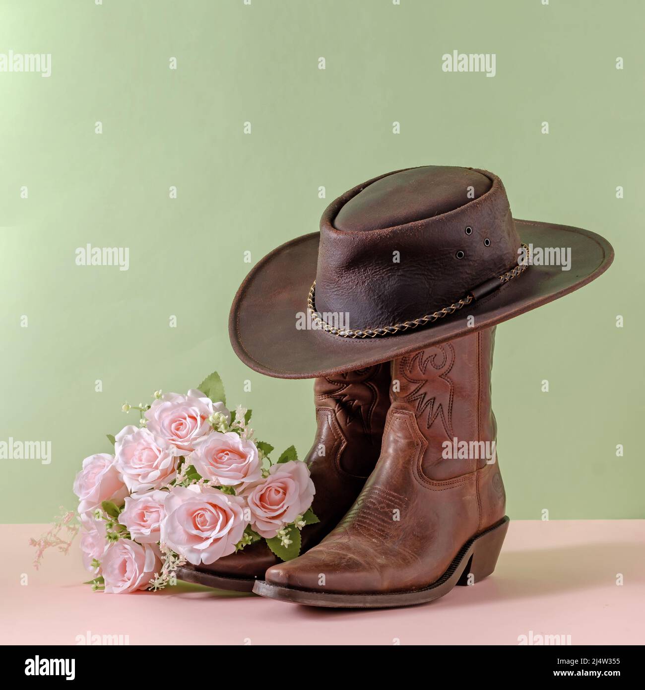 Cowboy boots shoes and hat and bouquet of rose flowers on green background minimal creative concept symbol of wild west america usa texas farm and par Stock Photo