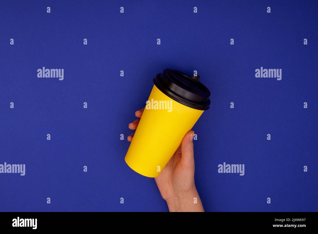 Paper cup of coffee in hand. Yellow paper cup of coffee in hand isolated mock up dark blue background Stock Photo